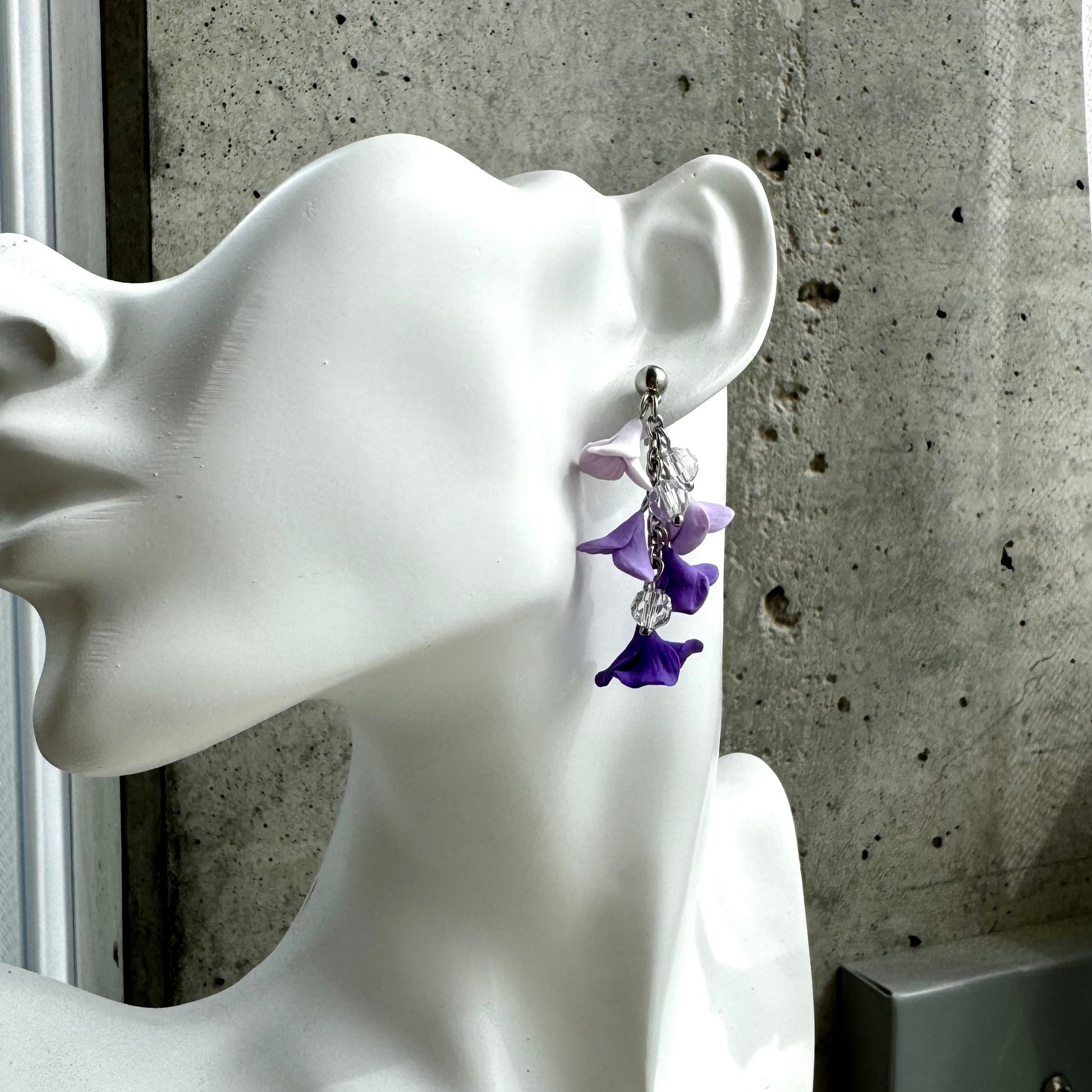 Kukkarimpsukorvakorut, joissa 5 kukkaa jonossa. Värit menevät lähes valkoisesta liukuvärjätysti tummaan violettiin. Seassa myös kristallilasihelmiä. Metalli hopeanväristä kiruginterästä.